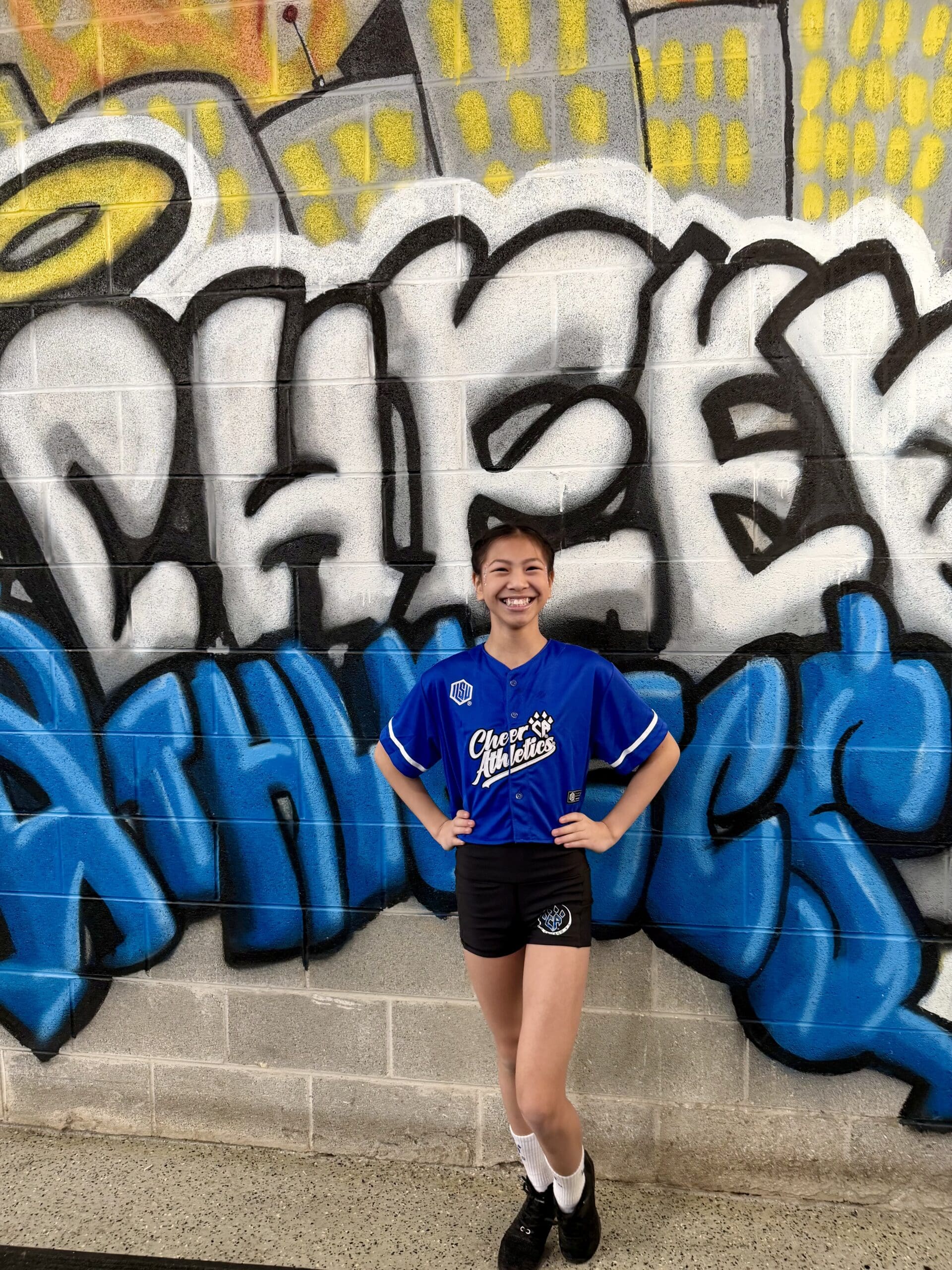 Roselyn posing in ILSVxCA in front of the colorful graffiti wall at Cheer Athletics Chicago.